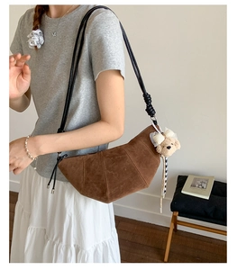 Detail of matte brown crescent bag with curved stitching and a cute plush bear charm