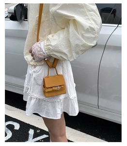 Detail of a yellow mini square bag featuring a flap closure and silver buckle strap decor