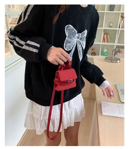 Close-up of a red mini leather bag with long shoulder strap worn by a model in scene