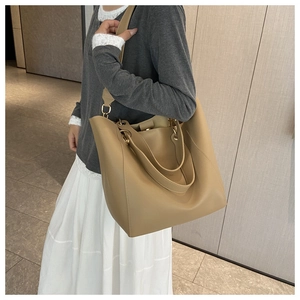 Side view of a khaki leather tote bag with gold hardware and adjustable strap on a model