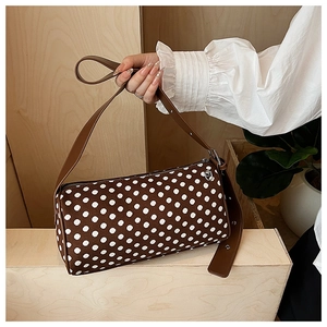 Detail of cylinder polka dot bag with leather strap on a wooden display stand