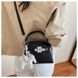 Detail of black croc-embossed mini Kelly bag with pearl strap and horse charm on model