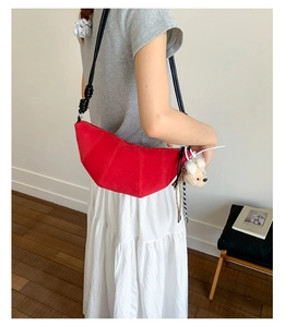 Detail of red suede crescent bag featuring knotted shoulder strap and plush bear charm