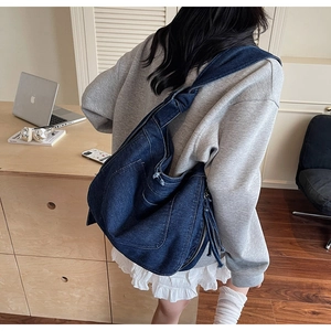 Detail of dark blue denim hobo bag with wide shoulder strap shown on a person