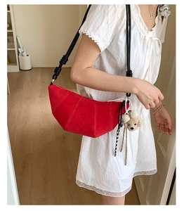 Detail of red suede croissant bag with thick knotted strap and plush bear charm