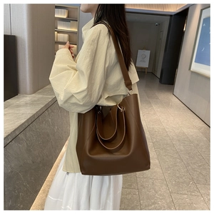 Detail of dark brown tote bag with wide shoulder strap and metal ring on model