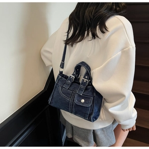Detail of dark blue denim tote bag showing stitching and metal buckle on model