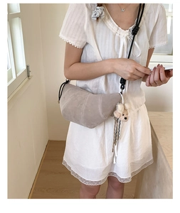 Detail of grey croissant bag featuring a braided black rope strap and plush bear charm