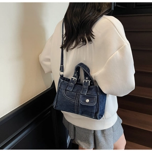 Detail shot of a dark blue denim crossbody bag featuring rustic buckles and pocket accents