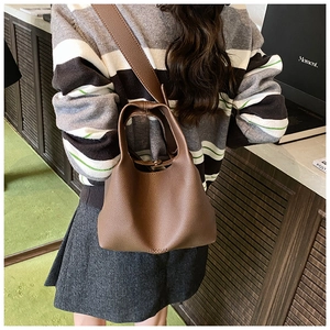 Detail of brown litchi leather bucket bag with HOCOMU logo and wide shoulder strap