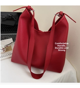 Close-up of red pebbled leather tote bag with wide handle on a desk with laptop