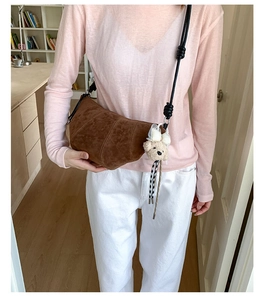 Detail view of brown suede croissant bag with woven strap and plush bear charm