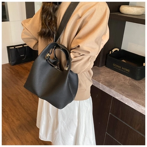 Detail of black lychee grain leather bucket bag with golden hardware and wide strap