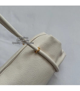 Macro shot of ivory pebble leather texture and gold metal ring hardware on the shoulder bag