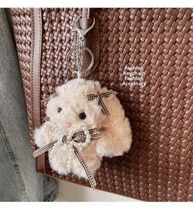 Detail of cute beige plush bunny keychain with pearl and plaid bow on a woven tote bag