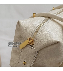 Close-up of textured cream leather shoulder bag featuring a smooth gold zipper closure