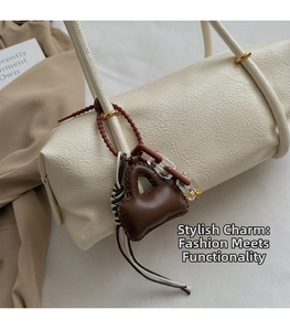 Detail of dark brown leather mini bag charm with acrylic chain on a cream shoulder bag