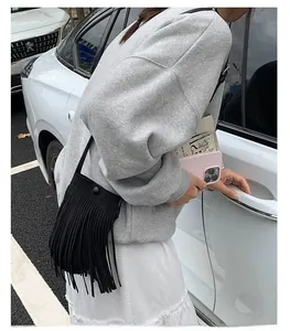 Détail d'un sac bandoulière noir à franges en daim porté par un mannequin en tenue décontractée