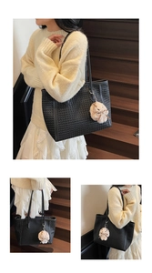 Detail view of black woven tote bag with cute beige plush bunny charm on wooden stairs