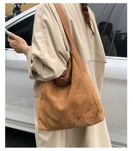 Détail du sac seau en daim marron avec l'écusson en cuir à quatre surpiqûres blanches