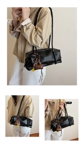 Detail of black cylindrical baguette bag in oiled leather texture with creative charms