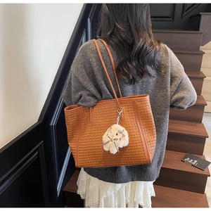 Detailed texture of brown woven tote bag with a cute white bunny charm and long straps