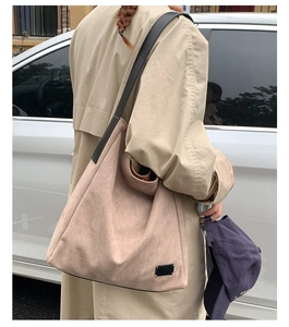 Détail du sac cabas en daim mat beige avec large bandoulière noire porté par un modèle