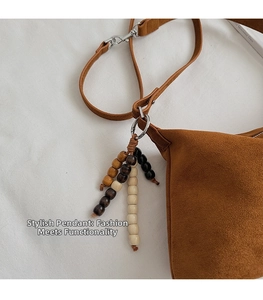 Detailed close-up of wooden bead tassel charm on brown suede crossbody bag