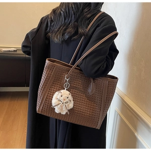 Detail of coffee brown woven tote bag featuring a plush rabbit pendant on a black coat model