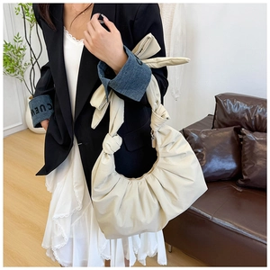 Close-up of beige pleated crescent bag with bow knot strap and soft leather texture