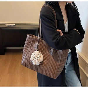 Detail of dark brown woven leather tote bag with a white plush rabbit pendant accessory