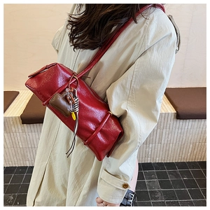 Detail of red cylindrical baguette bag in glossy patent leather with hanging ornaments