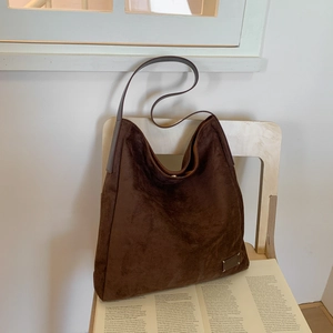 Detail of dark brown suede hobo bag with leather strap on a white wooden chair
