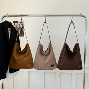 Minimalist large tote bags in brown and grey suede displayed on a metal rack