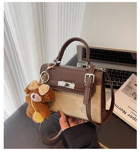 Nahaufnahme einer braun-beigen Handtasche im Kelly-Stil mit Plüschbären-Anhänger