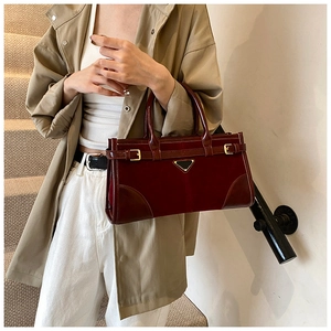 Detail of burgundy leather tote bag featuring a metallic triangle logo and decorative buckles