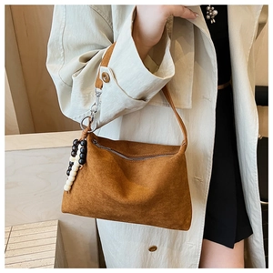 Detail view of brown suede underarm shoulder bag with beaded charm and zip closure.