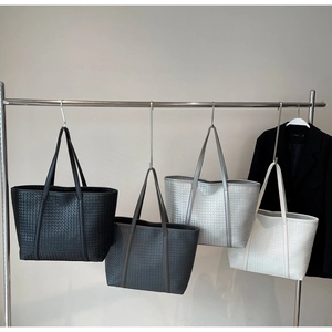 Minimalist large woven tote bags in four colors hanging on a metal rack display