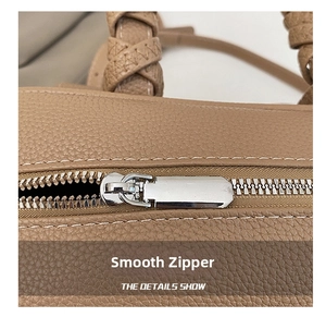 Detail of silver zipper closure and woven handle on brown lychee leather bag