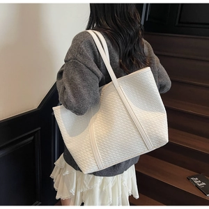 Detail of a woven cream tote bag showing the textured cross-weave pattern and long shoulder strap