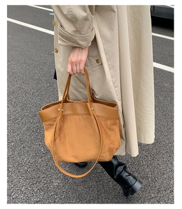 Detail of tan leather and suede patchwork tote bag paired with a beige trench coat