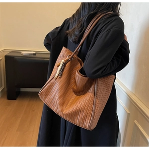 Brown woven tote bag with bead charm detail shown on a model in a minimalist setting