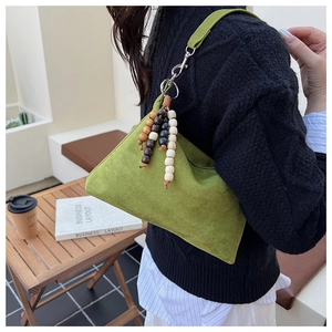 Detailed view of stylish green suede shoulder bag with wooden bead pendant on model. Fashion accessory.