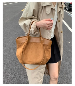 Detail of a brown tote bag featuring suede and leather patchwork with dual carry handles