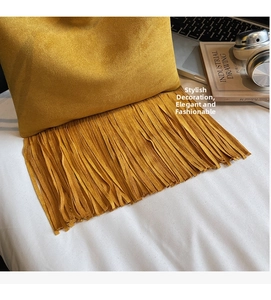 Detalle de bolso de ante amarillo con flecos bohemios junto a portátil y libros