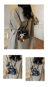 Detailansicht einer schwarzen Handtasche mit Bärenanhänger an einem Trenchcoat