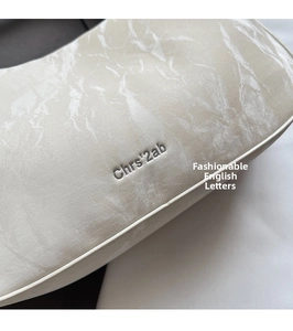 Detail shot of cream shoulder bag featuring marble texture and silver logo engraving