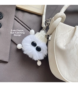 Macro shot of a cute white plush monster keychain with a knit hat on a marble bag