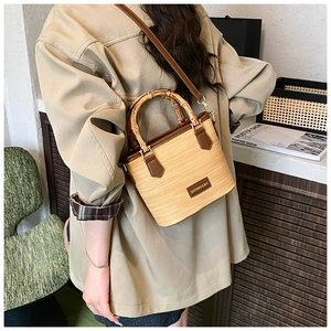 Detail of bamboo handle and leather trim on beige woven bucket bag for summer