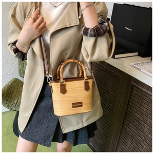 Detail of hand-woven straw bucket bag with bamboo handle and brown leather trim strap